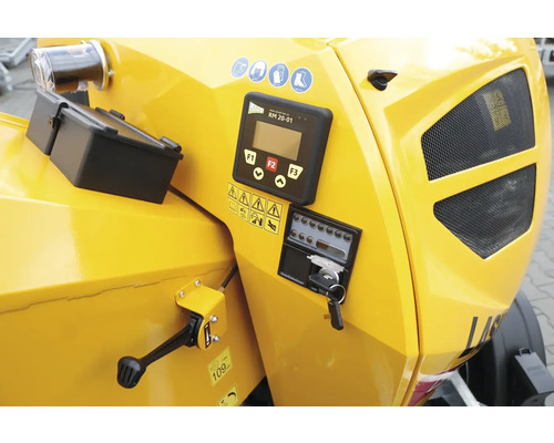 Nahaufnahme einer gelben Holzhackmaschine mit Bedienelementen und Sicherheitssymbolen