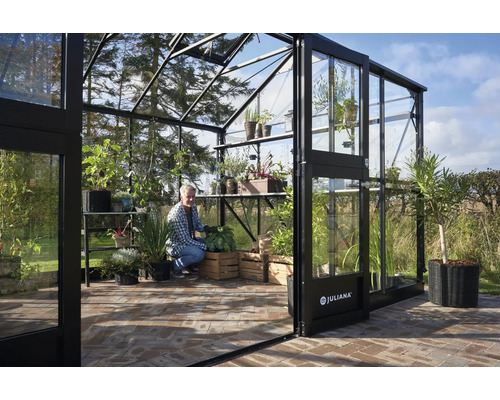 Serre spacieuse avec des plantes et un homme travaillant dans le jardin.