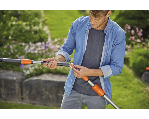 Un homme ajuste une rallonge de manche télescopique Gardena pour outils de jardin dans le jardin.