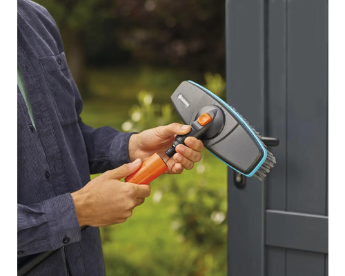 Une personne raccorde une brosse à un tuyau d''arrosage pour des travaux de nettoyage à l''extérieur.