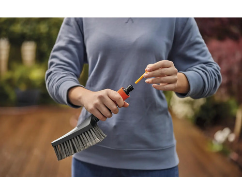 Une personne fixe un embout jaune à une brosse de nettoyage de jardin.