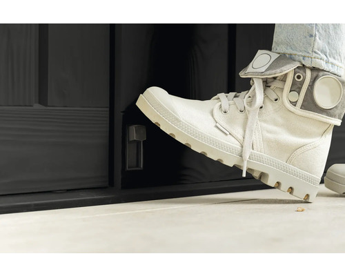 Person öffnet mit dem Fuß eine schwarze Außentür mit Drehknopf