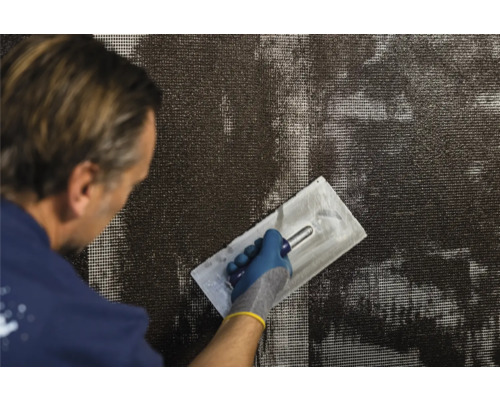 Ein Mann verputzt eine Wand mit Armierungsgewebe und einer Glättkelle.