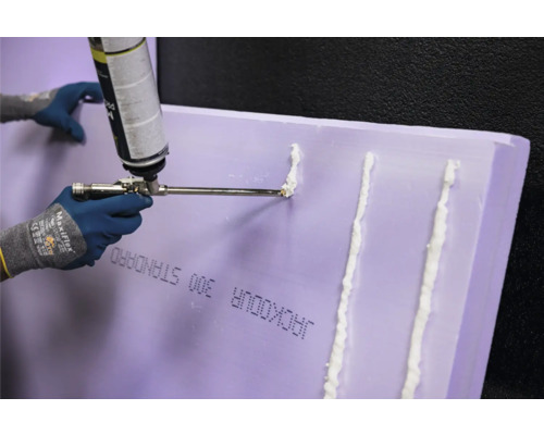 Person trägt Bauschaum auf eine Jackodur Dämmplatte auf