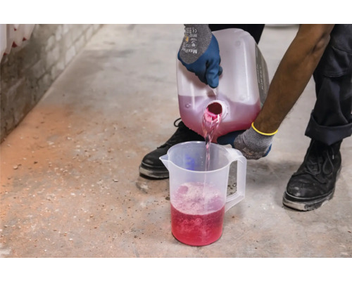 Eine Person gießt Flüssigkeit aus einem Behälter in einen Messbecher.