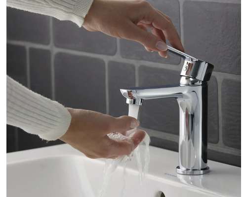 Person wäscht sich die Hände unter einem verchromten Wasserhahn an einem Waschbecken