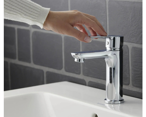 Hand betätigt Armatur auf einem Waschbecken im Badezimmer.