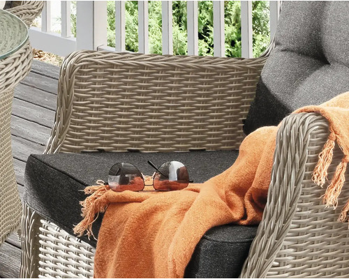Gros plan d''un fauteuil en osier avec coussin, d''une couverture et de lunettes de soleil sur une terrasse