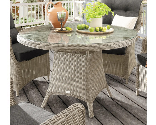 Table de jardin ronde avec plateau en verre et aspect rotin, entourée de chaises sur une terrasse