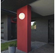 Runde Aussenleuchte an roter Säule vor einem Haus.