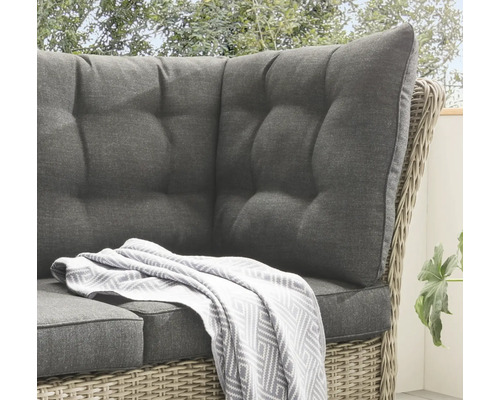 Detailansicht eines Rattansofas mit grauen Polstern und einer Decke