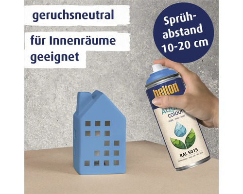 Eine Person sprüht mit einer blauen Farbspraydose ein blaues Hausmodell. Die Dose ist geruchsneutral und für Innenräume geeignet. Der Sprühabstand sollte 10 bis 20 Zentimeter betragen.