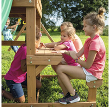 Kinder spielen auf einem Spielturm mit Tisch und Bänken im Garten.