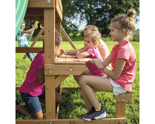Des enfants jouent sur une tour de jeux avec table et bancs dans le jardin.