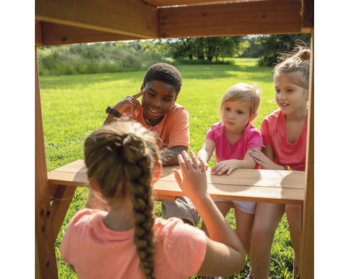 Des enfants sont assis à une table en bois à l''extérieur et interagissent les uns avec les autres.