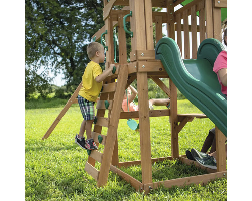 Un enfant grimpe sur une aire de jeux avec toboggan dans le jardin.