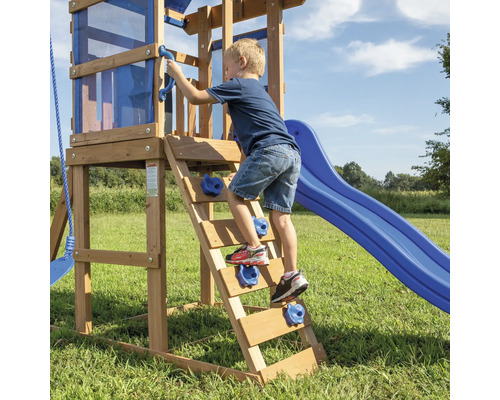 Garçon grimpant sur une tour de jeu en bois avec toboggan et mur d''escalade.