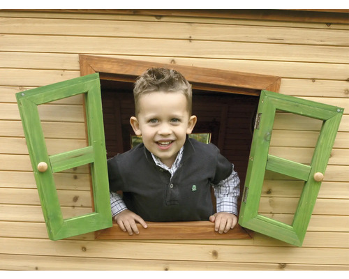 Ein Junge schaut aus dem grünen Fenster eines Holzspielhauses