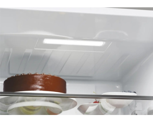 Innenansicht eines Kühlschranks mit Kuchen und Schale mit Beeren unter LED-Beleuchtung.