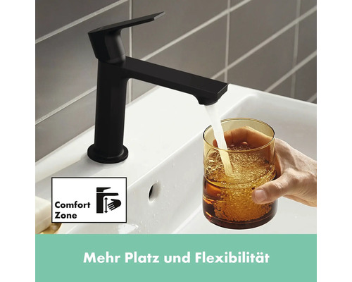 Schwarzer Wasserhahn mit Komfortzone füllt Glas mit Wasser im Waschbecken