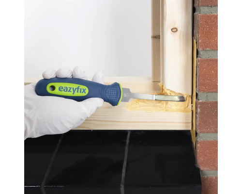 Une personne étanchéifie un cadre de fenêtre avec un grattoir à joints.