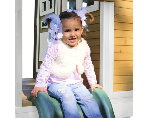 Mädchen rutscht auf einer grünen Rutsche vor einem Spielhaus