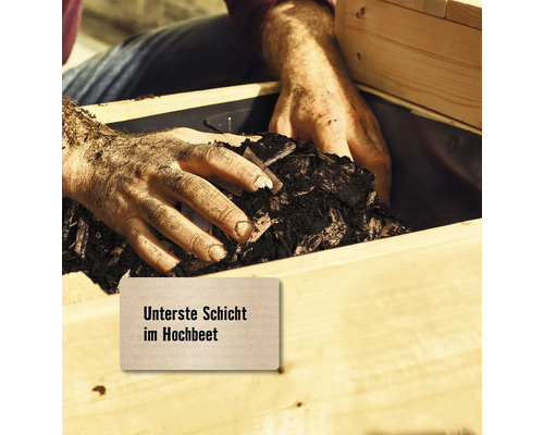 Hände füllen unterste Schicht in ein Hochbeet