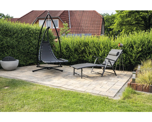 Gartenszene mit Hängekorbsessel, Liegestuhl und Feuerstelle auf einer gepflasterten Terrasse