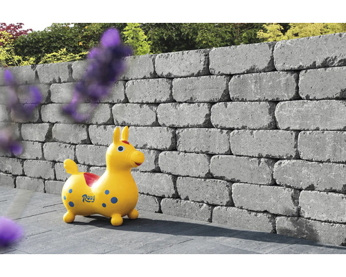 Des blocs de béton gris empilés forment un mur de jardin avec un jouet d''enfant devant.