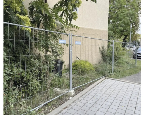 Baustellenzaun vor einem Gebäude mit Vegetation