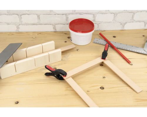Scène d''établi avec scie à onglets, scie à métaux, lattes en bois, serre-joints, crayon, équerre métallique et pot de peinture.
