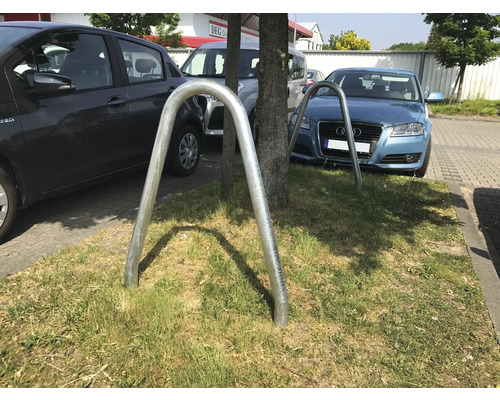 Zwei U-förmige Fahrradständer aus Metall auf einer Rasenfläche vor parkenden Autos.