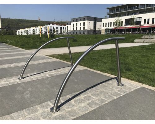 Deux supports à vélos incurvés en acier inoxydable sur une place pavée.