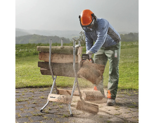 Eine Person sägt mit einer Kettensäge Holz auf einem Holzbock im Freien.