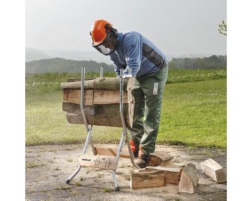 Eine Person arbeitet mit einem Holzsägebock zum Sägen von Holzstämmen in einem Außenbereich.