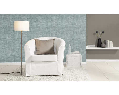 Wohnzimmer mit hellblauer Textiltapete, weißem Sessel und Stehlampe.