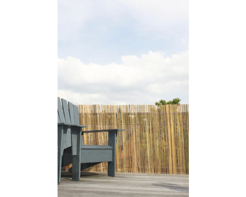 Scène avec une chaise de jardin grise et une clôture en bambou en arrière-plan.