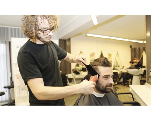Un coiffeur coupe les cheveux d''un client avec une tondeuse.