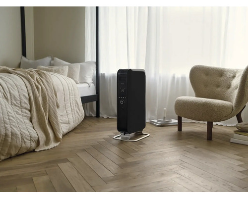 Schlafzimmer mit Bett, Sessel und einem schwarzen Heizkörper auf einem Holzfußboden.