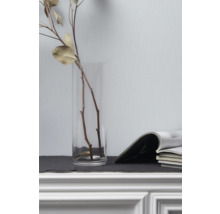 Branches décoratives dans un vase en verre à côté de magazines sur une commode