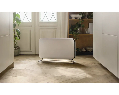 Radiateur blanc avec pied sur un plancher en bois dans une pièce lumineuse.