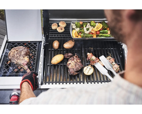 Un homme fait griller des steaks, des légumes et des pommes de terre sur un gril à gaz