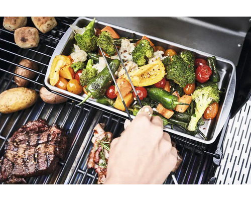 Gemüse und Steaks auf einem Grill zubereitet.