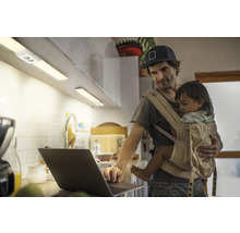 Mann mit Babytrage arbeitet am Laptop in der Küche mit Unterbauleuchten