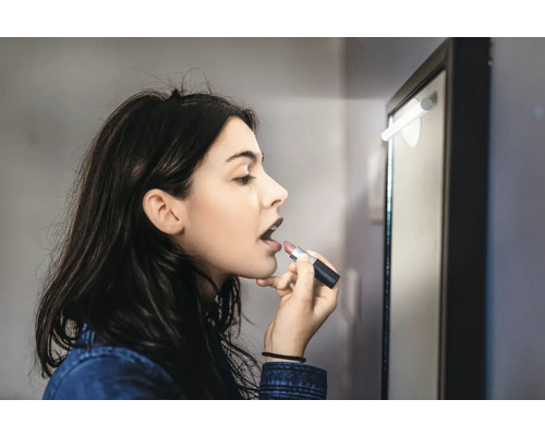 Eine Frau trägt Lippenstift vor einem beleuchteten Spiegel auf