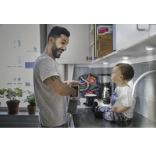 Vater und Kind in einer hellen Küche mit Unterbauleuchten, der Vater bereitet Toast zu.