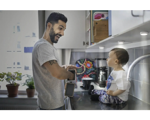 Vater und Kind in einer hellen Küche mit Unterbauleuchten, der Vater bereitet Toast zu.