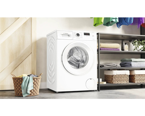 Weiße Bosch Waschmaschine in einem Wäscheraum mit Regalen, Körben und Wäsche.