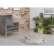 Wohnzimmer mit grauem Sessel, rundem Teppich und Zimmerpflanzen vor einer Backsteinwand.