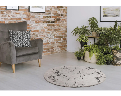 Wohnzimmer mit grauem Sessel, rundem Teppich und Zimmerpflanzen vor einer Backsteinwand.